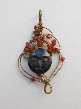 Antique brass wire pendant, red oak leaves behind a round black carved face